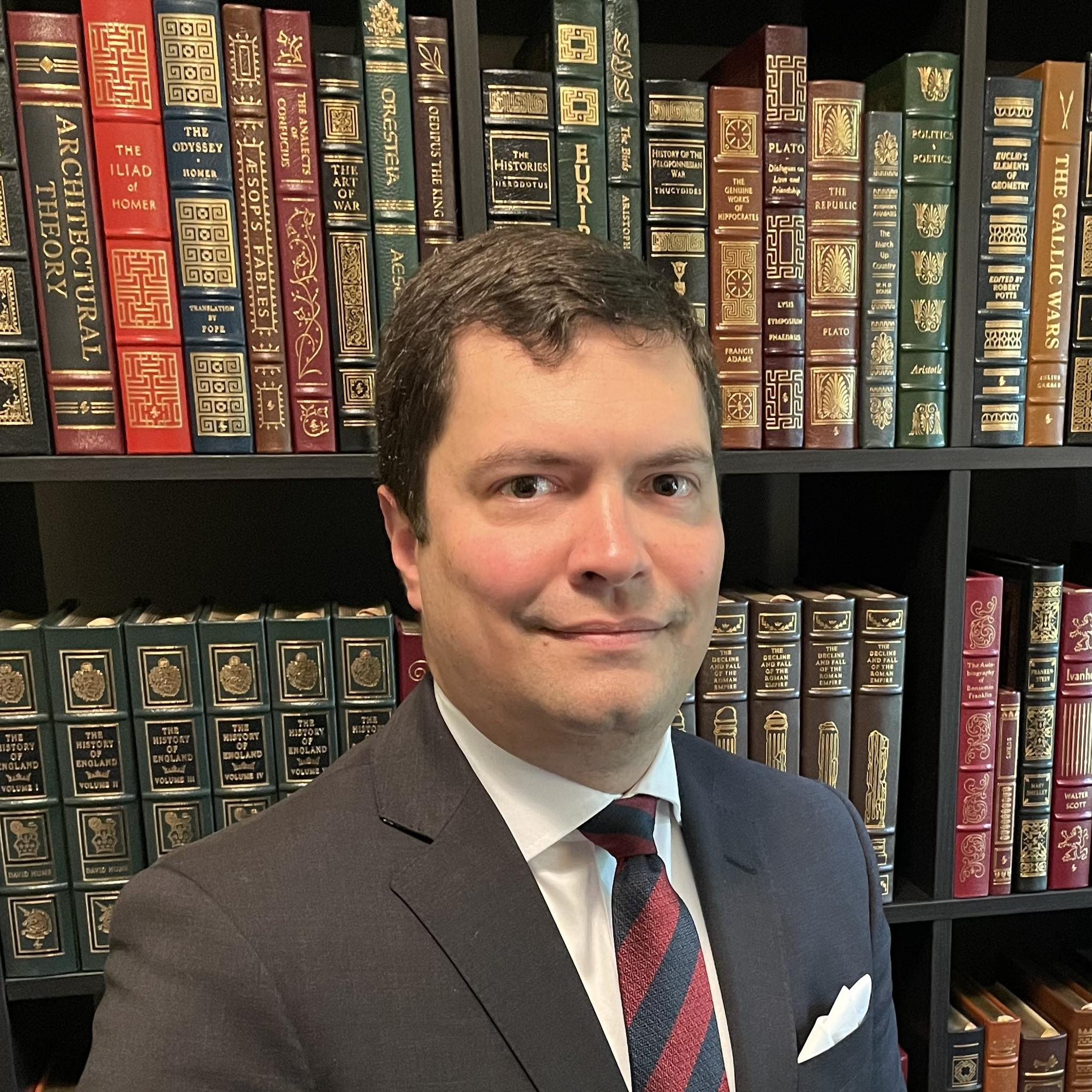 Dr Joseph Stoltz III in front of a library of leather bound classic books
